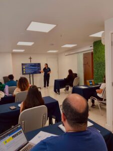 Sala de aula do Instituto Celebra durante a turma de Recertificação: a instrutora aponta para um slide com diretrizes para a prática enquanto profissionais acompanham sentados em mesas com apostilas e notebooks.