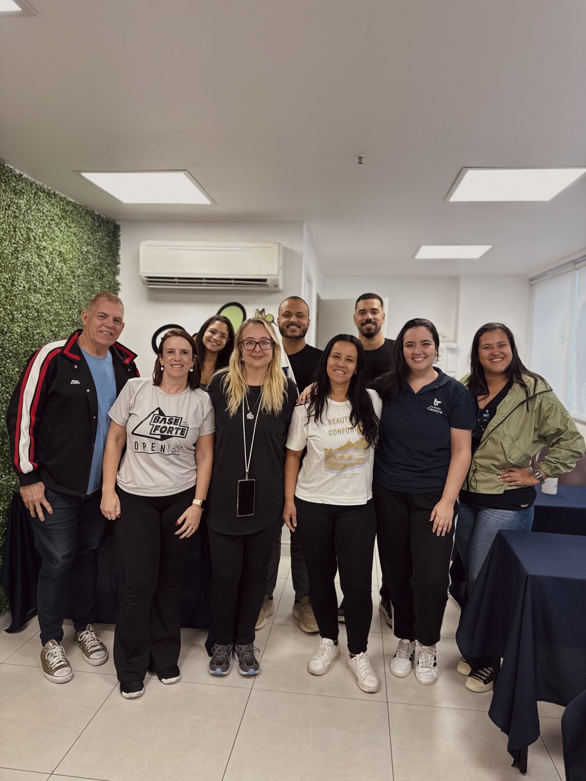 Turma da Certificação PCM de agosto de 2026 reunida na sede do Instituto Celebra: nove participantes sorrindo, lado a lado, em frente ao painel verde da sala de treinamento